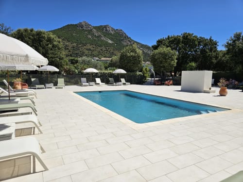 Hotel Les Mouettes pool terrace in Belgodère with lounge chairs, umbrellas, and mountain views