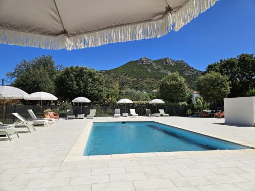 Luxury pool area at Hotel Les Mouettes in Belgodère with lounge chairs, white umbrellas, and mountain views