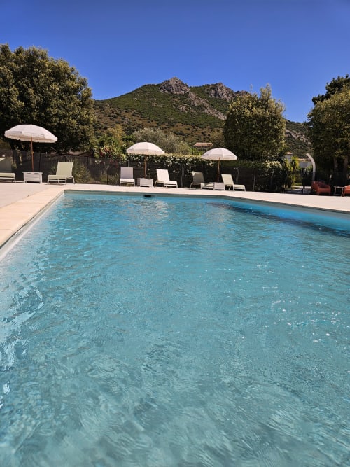 Sparkling pool with loungers and umbrellas at Hotel Les Mouettes, Belgodère, with mountain backdrop