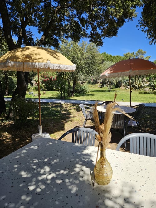 Hotel Les Mouettes outdoor patio with umbrellas, tables, and Mediterranean garden in Belgodère