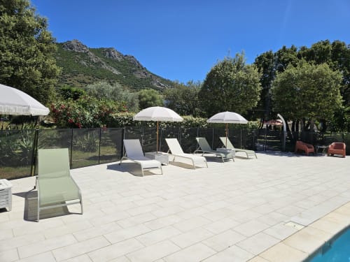 Sunny poolside patio at Hotel Les Mouettes in Belgodère with loungers, umbrellas, and mountain views