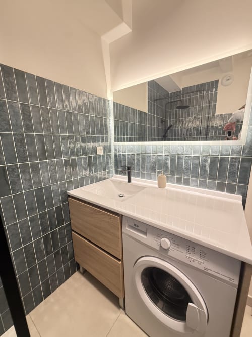 Salle de bain moderne avec murs carrelés noirs, lavabo blanc, machine à laver et miroir à l'appartement Mattbnb au Luxembourg