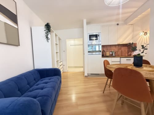 Séjour moderne à Mattbnb Luxembourg : canapé bleu, table à manger, cuisine blanche et parquet en bois
