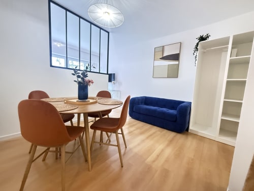 Salle à manger contemporaine de l'appartement Mattbnb Luxembourg avec table ronde en bois, chaises cognac, canapé bleu et vue sur la ville