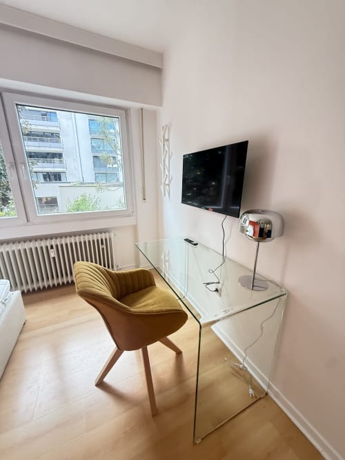 Espace de travail moderne à Luxembourg Limpertsberg avec TV écran plat, bureau en verre, chaise moutarde et vue sur la ville