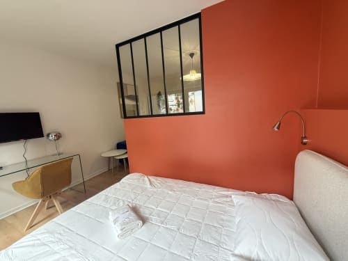 Chambre moderne avec mur d'accent orange, lit blanc, espace de travail et cloison vitrée à Mattbnb Luxembourg