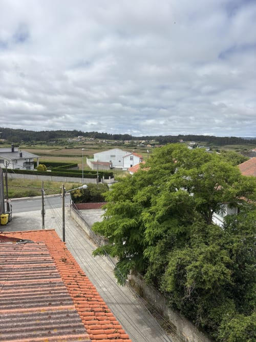 Vista del paisaje rural de Malpica desde Hotel Restaurante O Esqueiro con árbol verde, edificios y cielo nublado