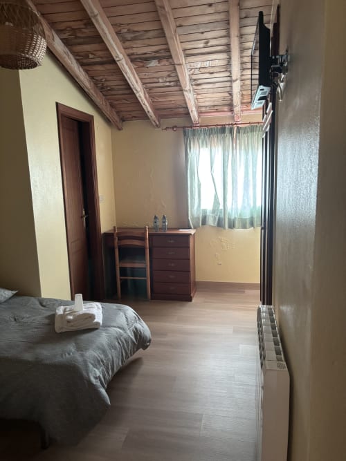 Bright bedroom at Hotel O Esqueiro in Malpica with wooden beams, garden view windows, desk, and wooden flooring