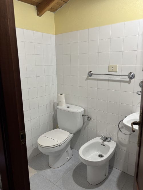 Clean white-tiled bathroom at Hotel O Esqueiro in Malpica with toilet, bidet, and sink fixtures