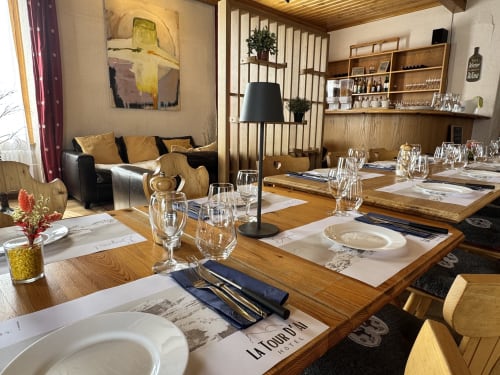 Salle à manger élégante de l'Hôtel La Tour d'Aï à Leysin avec tables en bois, couverts dressés et salon moderne.