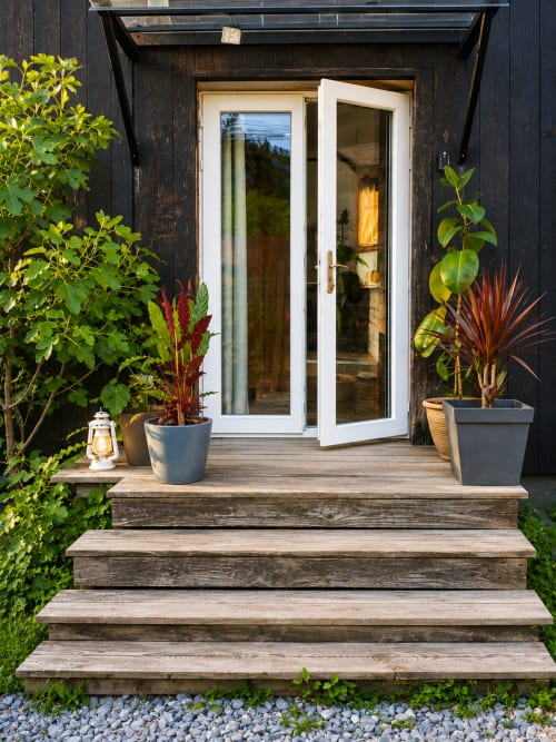 Entrée de mini-maison moderne au gîte de Chaparon avec portes blanches, terrasse en bois, plantes en pot et vue sur les montagnes