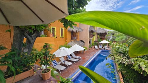 Patio de l'hôtel Ensueño De Fuga à Zihuatanejo avec piscine bleue, bâtiment orange, chaises longues et plantes tropicales