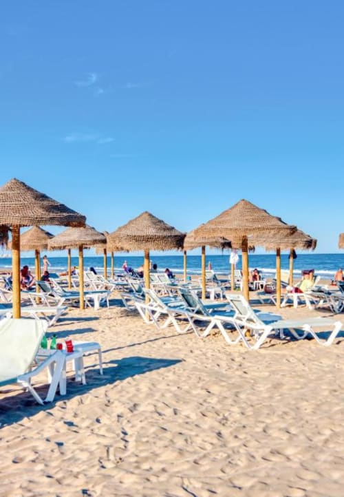 Beach lounge area in Valencia with thatched umbrellas, white sun loungers, and Mediterranean Sea view at Pataconablue Rentals