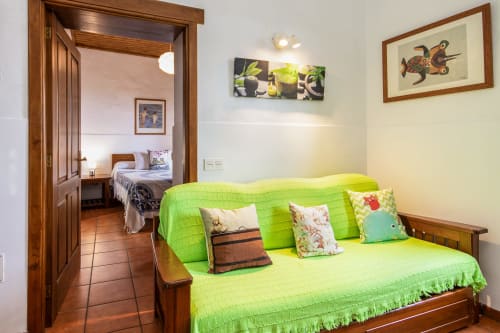 Sofá cama verde brillante con cojines coloridos en Apartamento Deluxe de Villanueva Lanzarote, mobiliario de madera visible