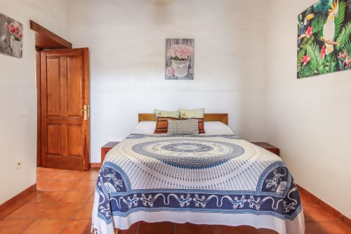 Dormitorio luminoso en apartamento de Villanueva Lanzarote con ropa de cama azul estampada, cabecero de madera, suelos de terracota y detalles florales