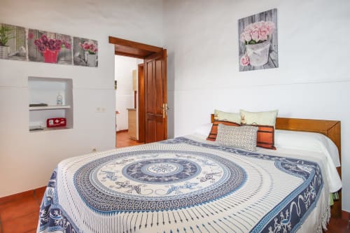 Habitación deluxe en Villanueva Lanzarote con cama de madera, ropa de cama azul estampada y arte floral en la pared