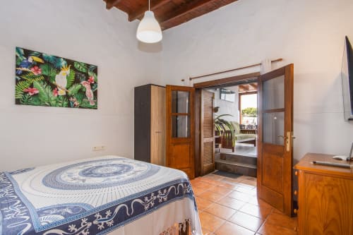 Dormitorio de apartamento de lujo en Villanueva Lanzarote con ropa de cama azul estampada, puertas de madera, vista al jardín y arte tropical