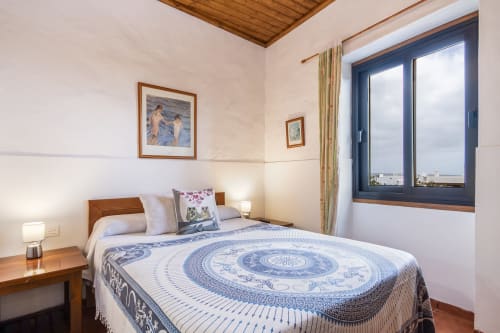 Dormitorio acogedor en Villanueva Lanzarote con colcha de patrón azul, muebles de madera y vistas al océano