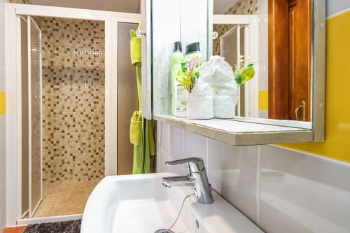Baño moderno en Villanueva Lanzarote con lavabo blanco, grifo cromado, espejo, toallas y ducha con azulejos mosaico