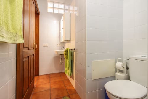 Baño moderno en Villanueva Lanzarote con baldosas de terracota, paredes alicatadas en blanco, puerta de madera y detalles verdes