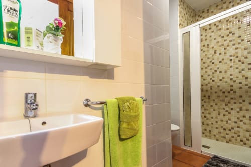 Baño moderno en apartamento de lujo Villanueva Lanzarote con lavamanos blanco, toallas verde lima y ducha de mosaico