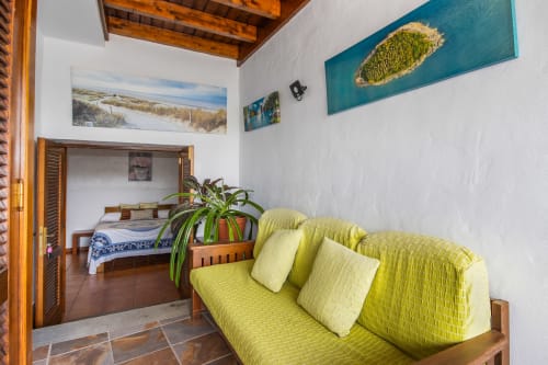 Luminosa sala de estar del Apartamento Deluxe Villanueva Lanzarote con sofá verde lima, planta en maceta y obra de arte costera en Mala