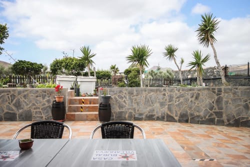Terraza de Villanueva Lanzarote con vistas al jardín, sillas negras, palmeras y muros de piedra en Mala