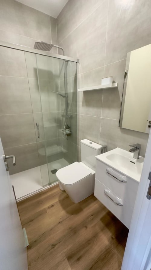 Banheiro moderno da suíte familiar Pink-Shell com chuveiro em vidro, cuba branca, vaso sanitário e piso de madeira