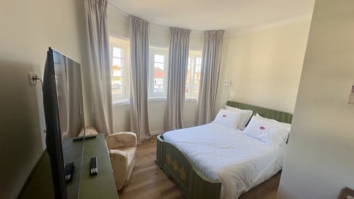 Suíte familiar moderna no Pink-Shell com cama de estrutura verde, roupas de cama brancas, janelas curvas com cortinas cinzentas e vistas para o jardim