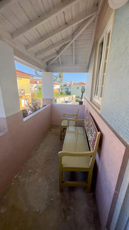Varanda coberta com duas cadeiras de madeira, paredes rosadas e vista para o jardim na Pink-Shell BnB em Santiago de Riba-UI