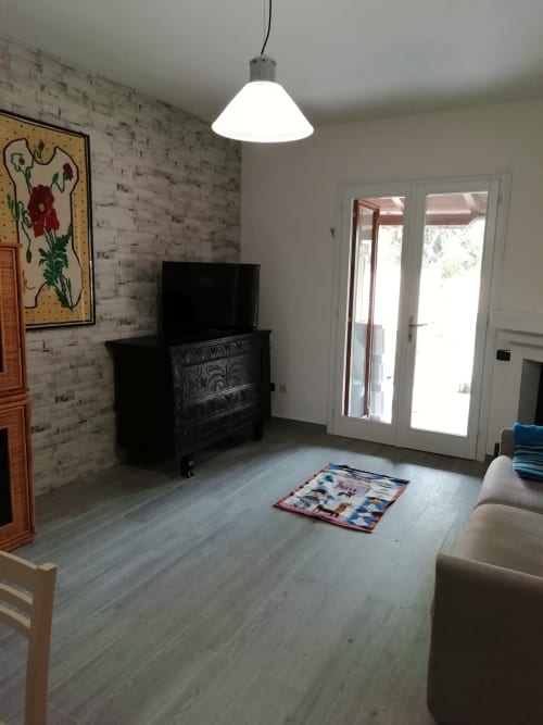 Soggiorno moderno in Villa Acquamarina con muri in laterizio bianco, TV schermo piatto, luci sospese e porte con vista sul giardino
