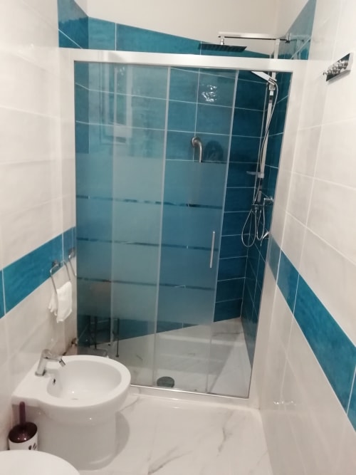 Bagno moderno con doccia in vetro, lavabo bianco, wc e dettagli in piastrelle turchesi a Villa Acquamarina, Quartu