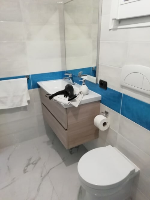 Bagno moderno in Villa Acquamarina con wc bianco, mobile bagno in legno, dettagli in piastrelle blu e specchio presso House Live