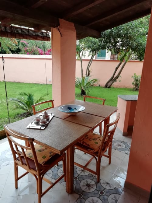 Covered terrace dining area at Villa Acquamarina with wooden table and chairs overlooking lush garden, Quartu Sant'Elena