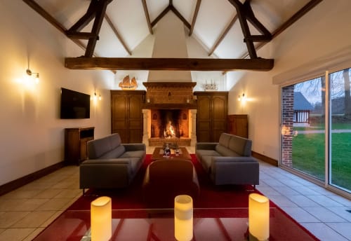 Élégant salon avec cheminée au Clos Céleste : poutres apparentes, canapés modernes, piliers lumineux et vue sur le jardin en Normandie