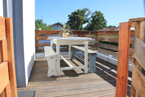 Terrasse ensoleillée du gîte Le Grand Bain avec table à manger blanche, chaises et plante en pot donnant sur la piscine de La Pause