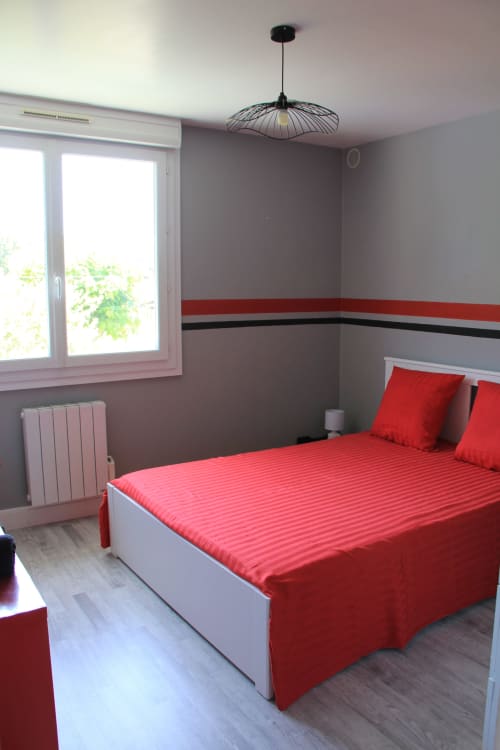 Chambre moderne à La Pause Landaise avec literie rayée rouge, murs gris, luminaire suspendu et vue sur la piscine