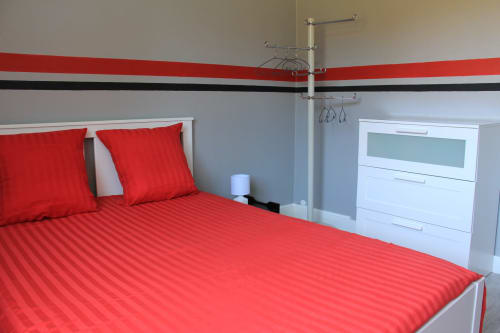 Chambre moderne avec literie rouge et mobilier blanc au gîte La Pause Landaise à Magescq, France