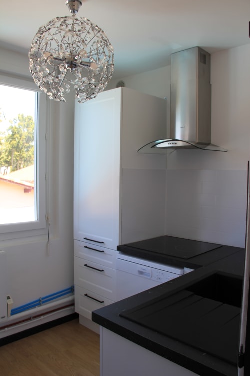 Cuisine moderne avec plan de travail noir, cabinetry blanc, hotte inox et suspension en cristal à La Pause Landaise