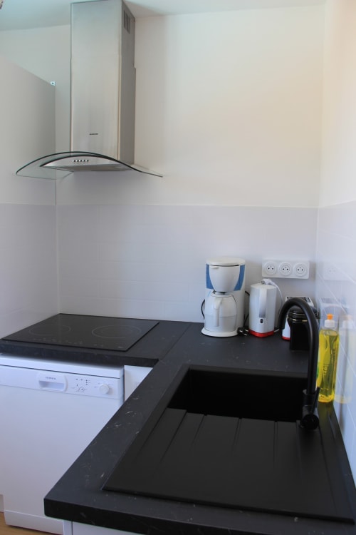Cuisine moderne du cottage Le Grand Bain à La Pause Landaise : plan de travail noir, plaque induction et acier inoxydable