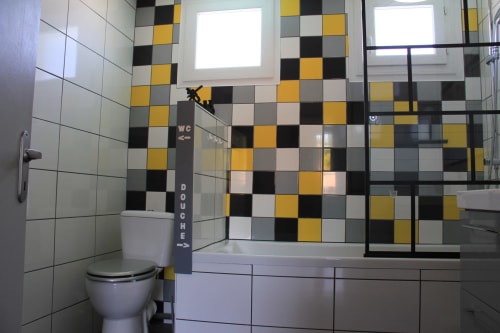 Salle de bains moderne aux carreaux damier noir, blanc et jaune, toilettes, lavabo et douche vitrée à La Pause Landaise