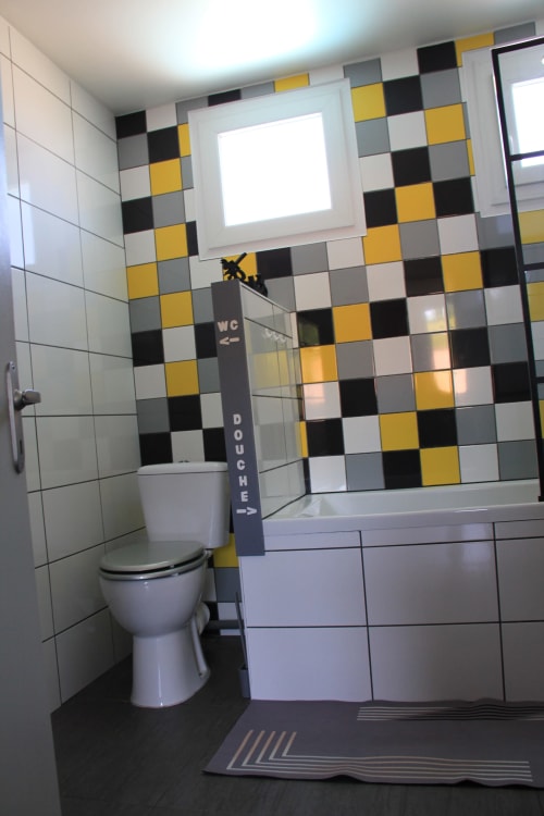 Salle de bains moderne du gîte Le Grand Bain à La Pause Landaise, aux murs carrelés avec motifs géométriques jaune, noir et blanc