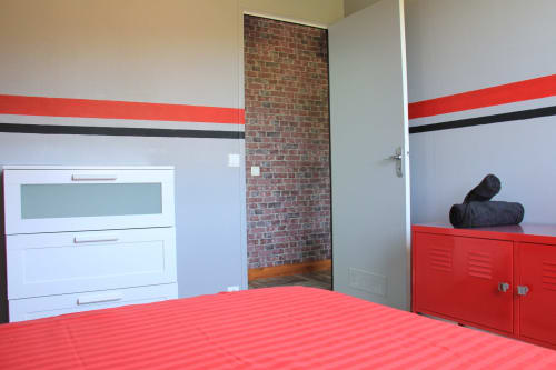 Chambre moderne à La Pause Landaise avec mur à rayures rouges et noires, mobilier blanc et rouge, briques apparentes