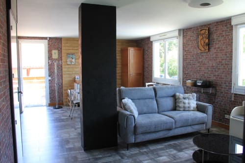 Séjour moderne du gîte Le Grand Bain à La Pause Landaise : canapé bleu, murs en brique, colonne noire et vue sur la piscine