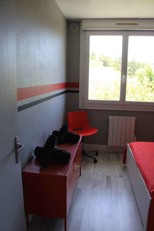 Chambre moderne du gîte La Pause Landaise avec murs à rayures rouges, lit aux draps rouges, bureau, chaise et vue sur le jardin