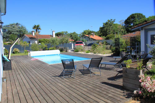 Piscine extérieure et terrasse en bois du gîte La Pause Landaise à Magescq, France, avec chaises longues et vue sur le jardin