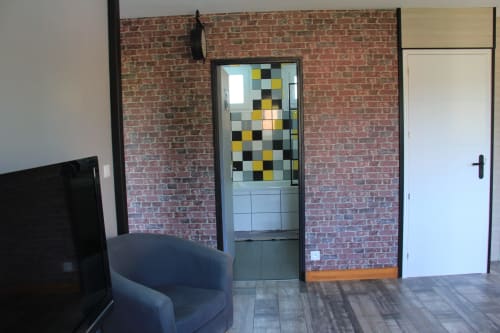 Intérieur de cottage moderne à La Pause Landaise avec murs en briques apparentes, porte géométrique colorée, chaise bleue et parquet