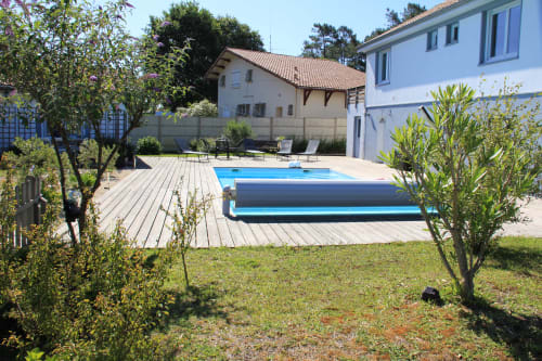 Le cottage Le Grand Bain de La Pause Landaise avec bâche de piscine, terrasse en bois, jardin et bâtiments aux volets bleus à Magescq