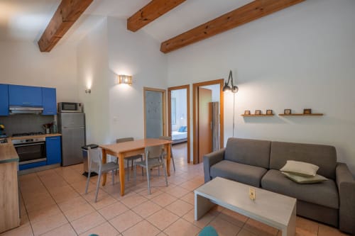 Salon moderne d'une villa à Propriano avec cuisine bleue, table à manger, canapé gris et poutres en bois