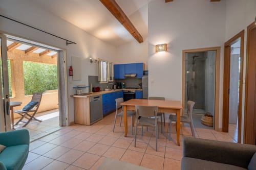Cuisine ouverte moderne et salle à manger de la villa de Propriano avec armoires bleues, poutres en bois, accès à la terrasse et jardin
